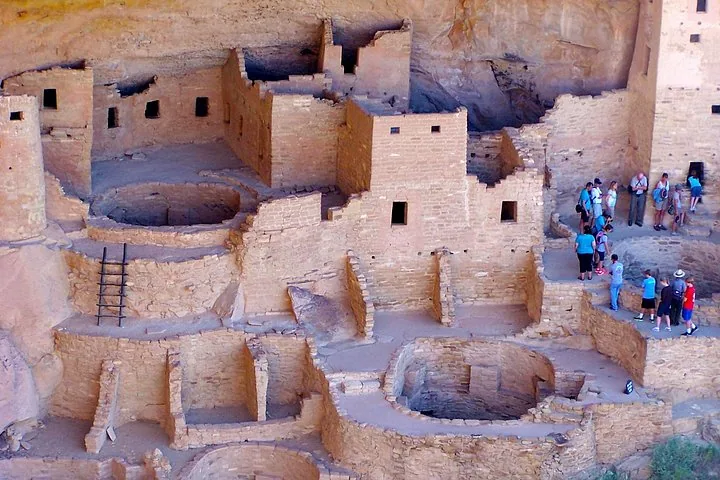 Turisti che esplorano antiche abitazioni rupestri a più piani con kivas circolari.