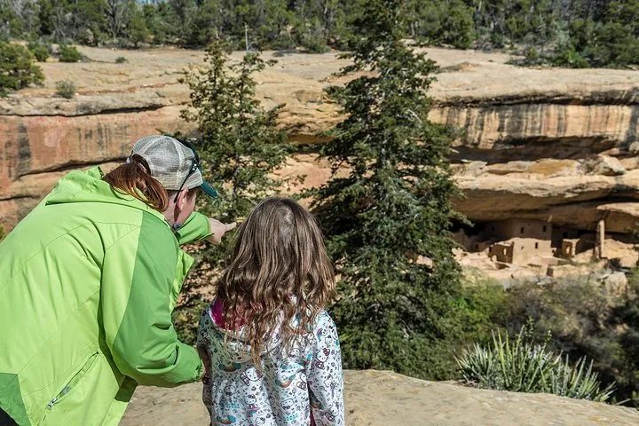 Una donna e un bambino guardano le abitazioni rupestri dall'altra parte di un canyon.